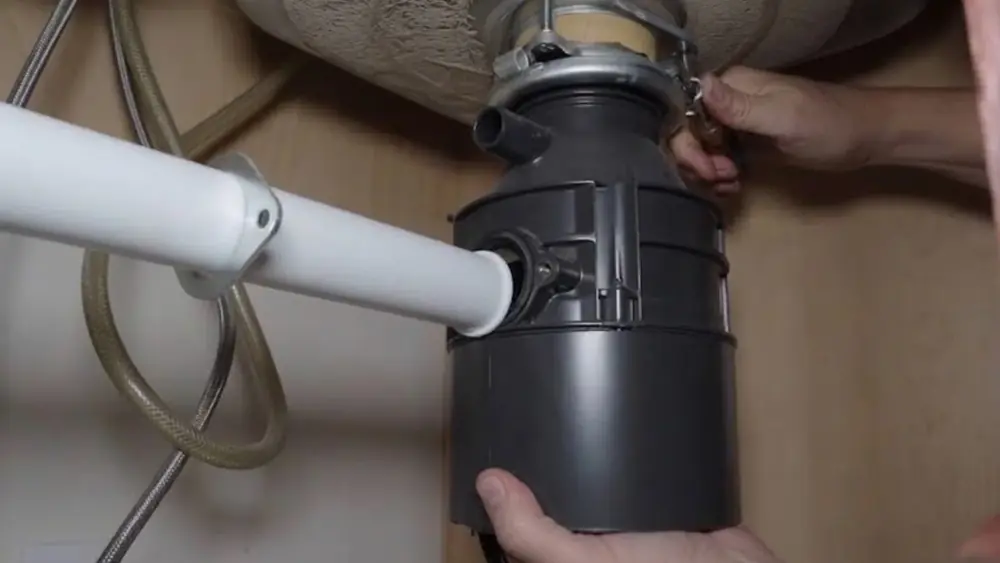 Hands fitting a drain pipe to a garbage disposal